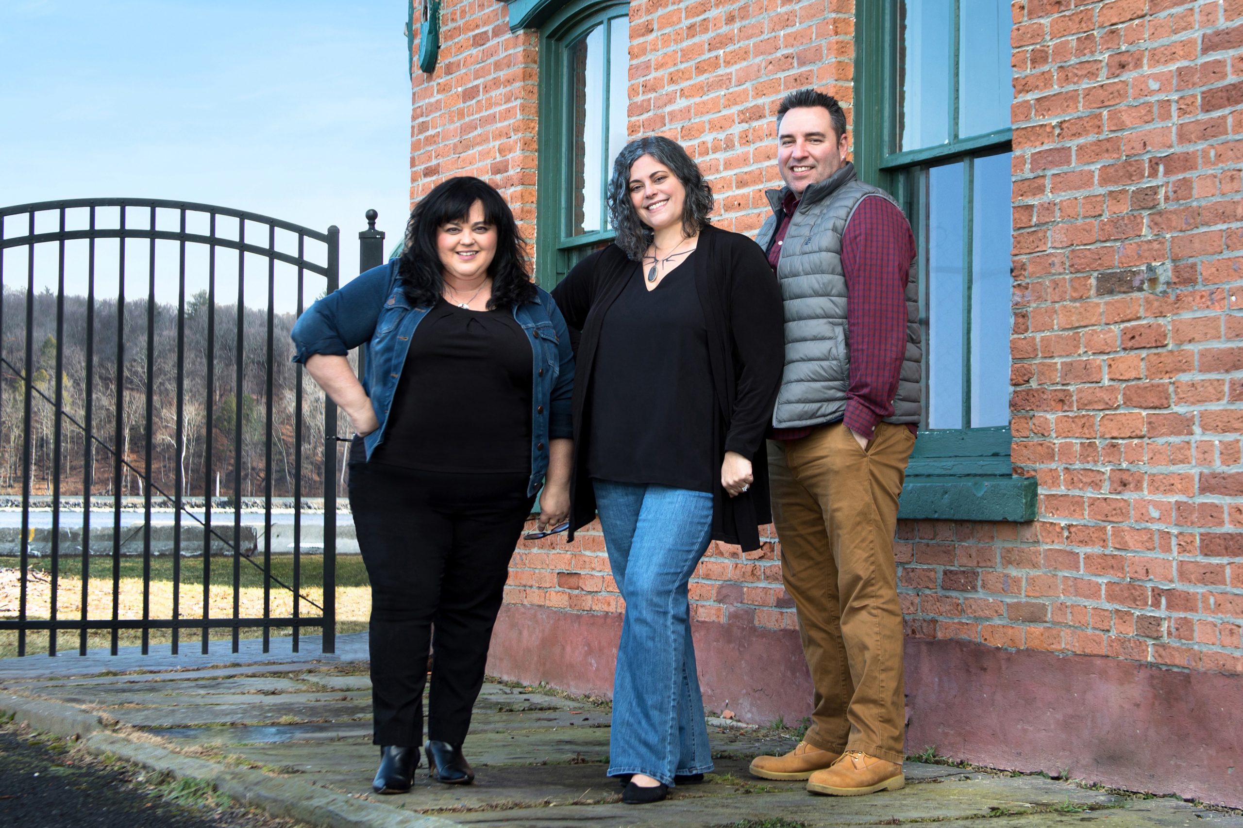 Angela Lanuto, Allison Morelle, and Jason Weiner of The Angela Lanuto Team At Village Green Realty smiling against brick building